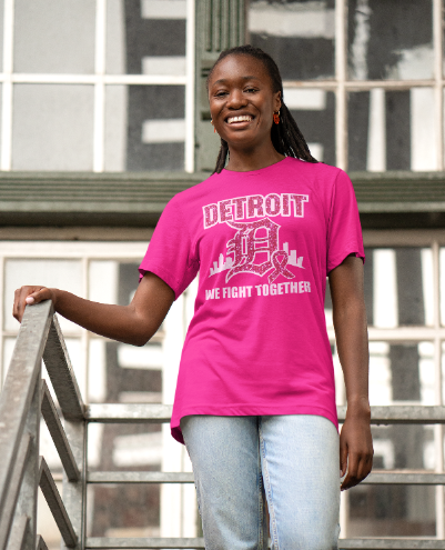 Person wearing a pink t-shirt with 'Detroit We Fight Together' text and graphic, standing outdoors.